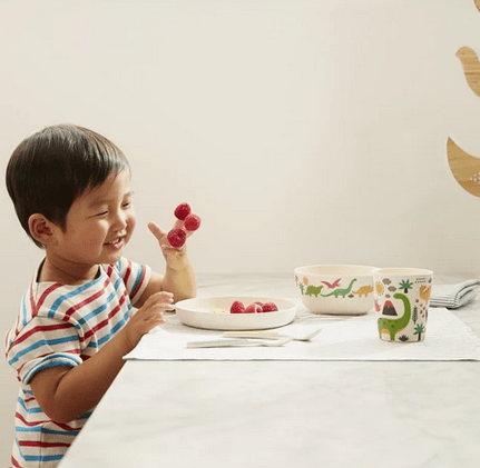 Child Using Petit Collage Bamboo Dinnerware Set in Dinosaurs